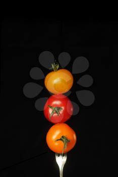 Tomatoes on a fork in a different colours on a black background