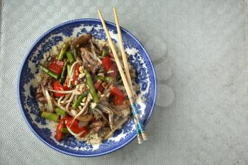 Colored vegetables saute in a blue bowl and chopsticks on a textured background
