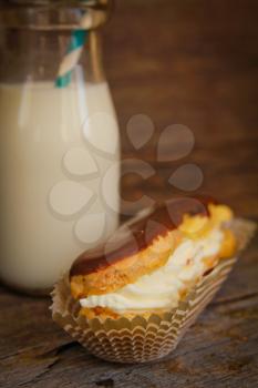 Close up of a chocolate eclair in a paper and an old fashion bottle of milk on a wooden surface