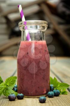 Jar containing blueberry smoothie with lined straw and fresh fruits
