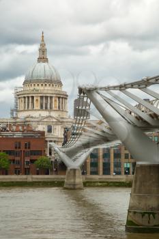 Tourists walking across the Millennium bridge to St. Paul Cathedral by a cloudy day in London