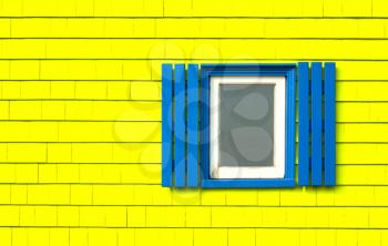 Traditional window with blue shutters on a bright yellow wooden tiles wall in Iles de la Madeleine in Quebec, Canada