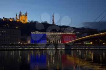 The historic courthouse of Lyon with the colors of France flag with  Basilica of Fourviere over the soane in background at sunset.