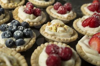 Blueberry, strawberry and pistachios tartlets on a wooden table