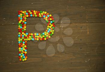 Letter P from alphabet made with star shape candy on a wooden background
