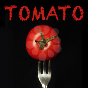 Red tomato facing us on a fork on a black background