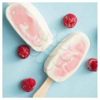 Two berry sorbet and yogurt popsicle with raspberry on a pale blue background with a white frame