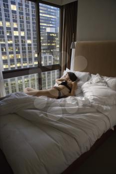 Royalty Free Photo of a Woman Wearing Lingerie Lying in a Bed Looking Out the Window at the Cityscape