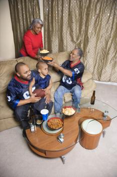 Mother serving snacks to male African-American family members during football game. 