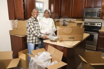 Portrait of middle-aged African-American couple packing moving boxes in kitchen.