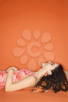 Smiling young Caucasian woman lying on floor with pillow on orange background.