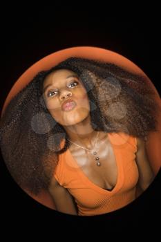 Vignette of young African-American adult woman with big hair and low cut dress on orange background puckering her lips.