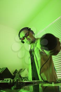 Royalty Free Photo of a Male DJ Standing Behind Mixing Equipment and Turntable Holding a Microphone Out