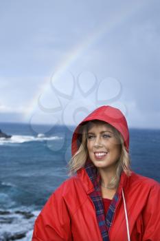 Royalty Free Photo of a Woman in a Red Raincoat in Front of an Ocean With a Rainbow and Smiling in Maui, Hawaii