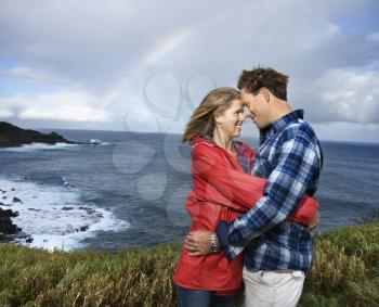Royalty Free Photo of a Couple Embracing By the Ocean With a Rainbow in the Background in Maui, Hawaii
