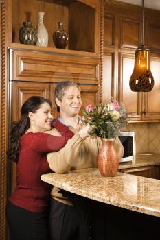Royalty Free Photo of a Woman Leaning on a Man While He Arranges Flowers in a Vase in the Kitchen