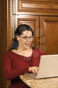 Royalty Free Photo of a Woman Typing on a Laptop in the Kitchen