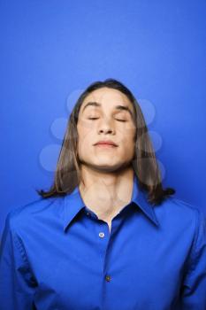 Royalty Free Photo of a Teen Boy Standing Against a Blue Background With His Eyes Closed
