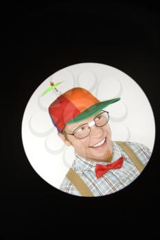 Close up circle vignett of Caucasian young man dressed like nerd wearing propeller hat looking mischievous.