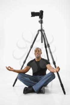 Royalty Free Photo of a Young Man Sitting Meditating Under a Camera and Tripod