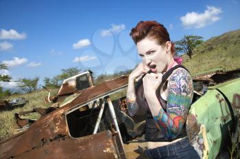 Angry tattooed Caucasian woman with fists clenched ready to fight in junkyard.