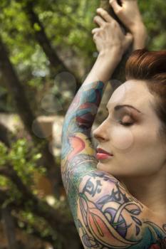 Royalty Free Photo of a Tattooed Woman in a Forest Leaning on a Tree in Maui, Hawaii, USA