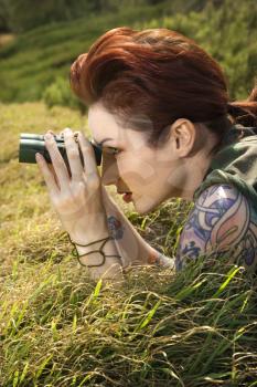 Royalty Free Photo of a Tattooed Woman Lying on Grass Looking Through Binoculars in Maui, Hawaii, USA