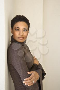 African-American woman standing leaning against wall looking at viewer.
