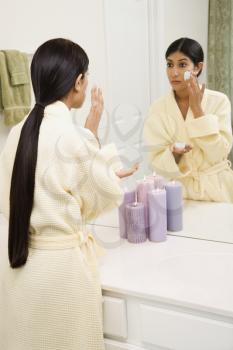 Royalty Free Photo of a Young Woman Looking in the Mirror Applying a Facial Scrub