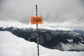 Ski area trail boundary sign with mountain landscape in background.