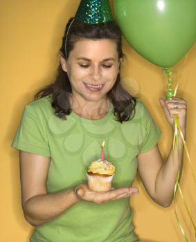 Royalty Free Photo of a Woman Holding a Cupcake With a Lit Candle Wearing a Party Hat