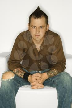 Royalty Free Photo of a Man With a Mohawk Sitting With Hands Clasped Together