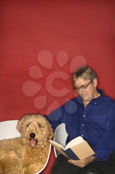 Royalty Free Photo of a Man Sitting With a Golden Doodle Dog and Reading a Book
