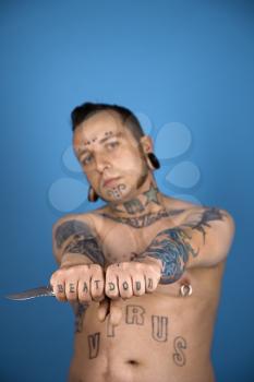 Barechested Caucasian mid-adult man with tattoos and piercings holding knife.
