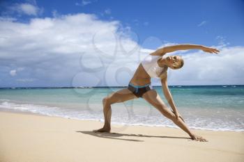 Caucasian young adult woman stretching on beach.