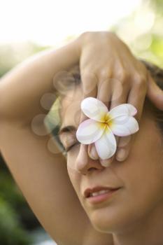 Royalty Free Photo of a Woman Holding a Plumeria Flower Over Her Eye