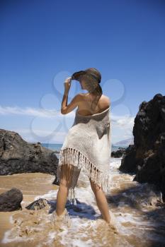 Royalty Free Photo of a Woman Standing in water on beach tilting brimmed hat