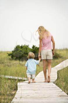 Caucasian pre-teen girl walking on beach access walkway and holding hands with Caucasian male toddler .