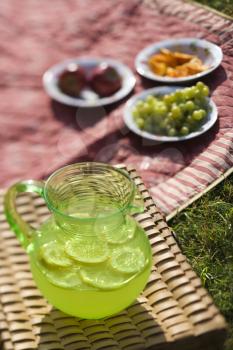 Royalty Free Photo of a Green Plastic Pitcher of Lemonade and Lemons With a Picnic Spread Out 
