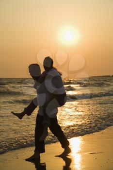 Royalty Free Photo of a Man Giving a Woman a Piggyback on the Beach at Sunset