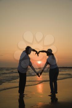Royalty Free Photo of a Couple Making a Heart Shape With Their Arms on a Beach at Sunset