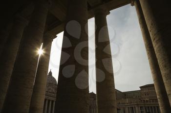 Royalty Free Photo of the Sun Peeking Through Doric Columns in Saint Peter's Square in Vatican City, Italy