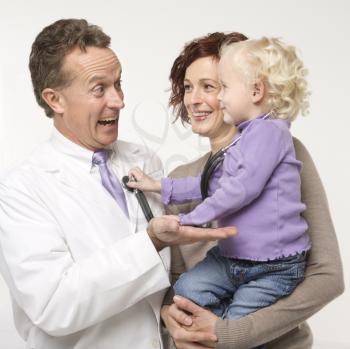 Royalty Free Photo of a Female Toddler Holding a Stethoscope Up to a Smiling Mae Doctor