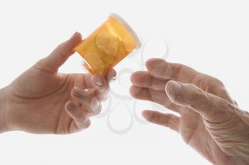 Royalty Free Photo of a Female's Hand Handing a Medication Bottle to an Elderly Male Hand