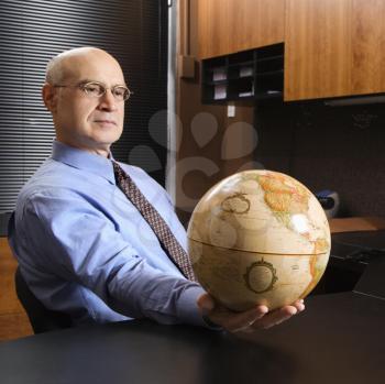 Royalty Free Photo of a Middle-aged Businessman Sitting at a Desk in an Office Holding a Globe