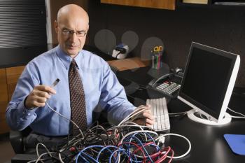 Royalty Free Photo of a Businessman at a Desk in an Office with a Tangle of Computer Cables