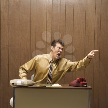Royalty Free Photo of a Businessman Sitting at a Desk Pointing in Anger