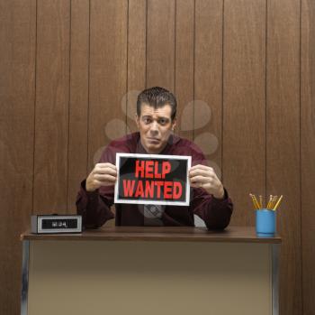 Royalty Free Photo of a Businessman Sitting at a Desk Holding a Help Wanted Sign