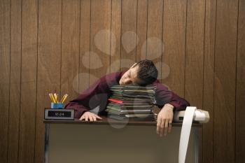 Royalty Free Photo of a Businessman Sitting at a Desk Resting His Head on a Tall Stack of Folders