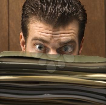 Royalty Free Photo of a Businessman Peering With Wide Eyes Over a Tall Stack of Folders